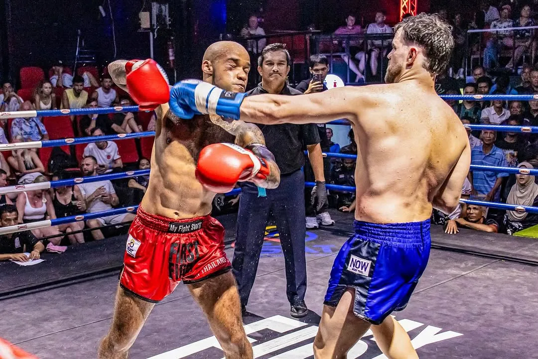 Two fighters trading punches at range in the ring, the referee and a packed crowd behind them.