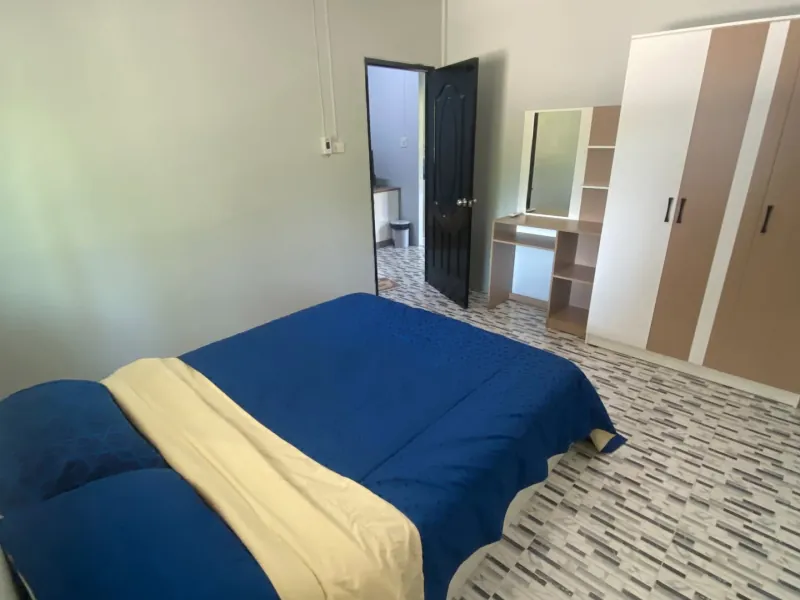 The bedroom of the private house: a double bed made up in blue, a dressing table and a full-height wardrobe, with the bathroom door open beyond.