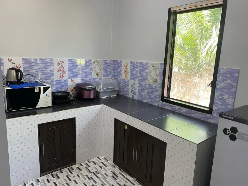 The kitchen of the private house: a tiled corner counter with a kettle, microwave, hotplate and rice cooker, and a window over the worktop.