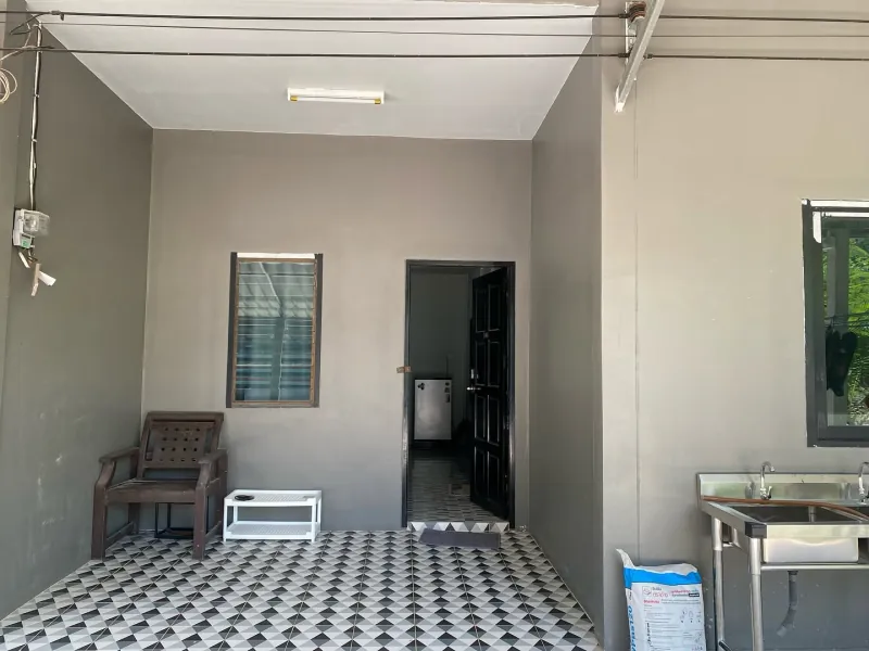 The covered porch outside the private house, with an outdoor sink, a wooden chair and the door through to the kitchen.