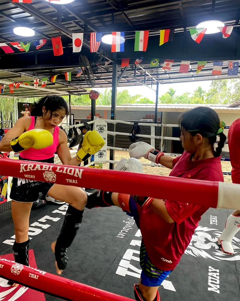 Two fighters sparring in the covered ring, gloves up as a kick comes in, national flags strung overhead.